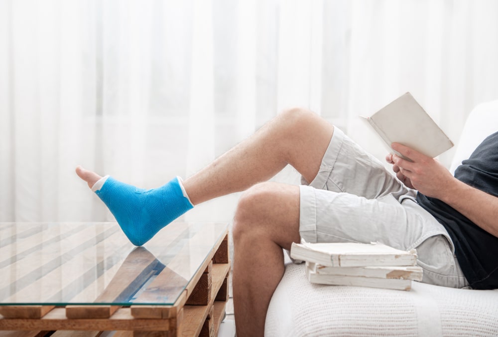 man-with-broken-leg-cast-reads-books-against-light-background-interior-room